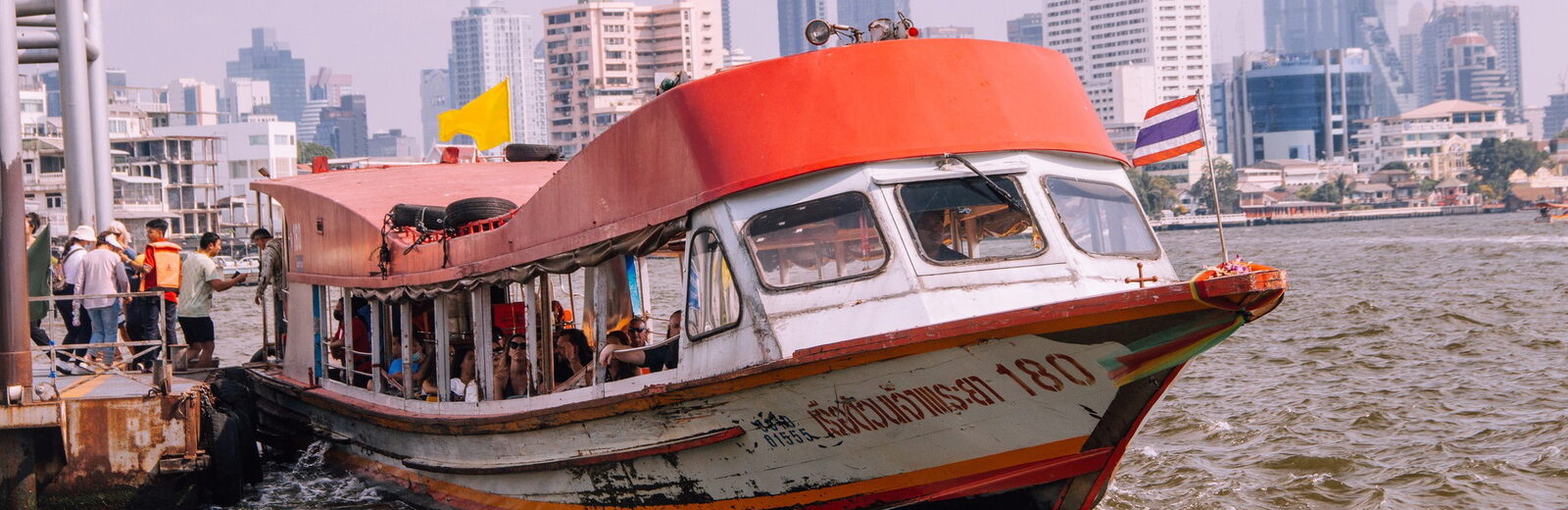 A Chao Phraya express boat on the river with the Bangkok skyline behind it